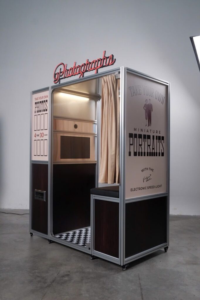 Inside the Vintage Booth enclosed photo booth showing the camera window, wooden bench, curtain, and checkerboard floor